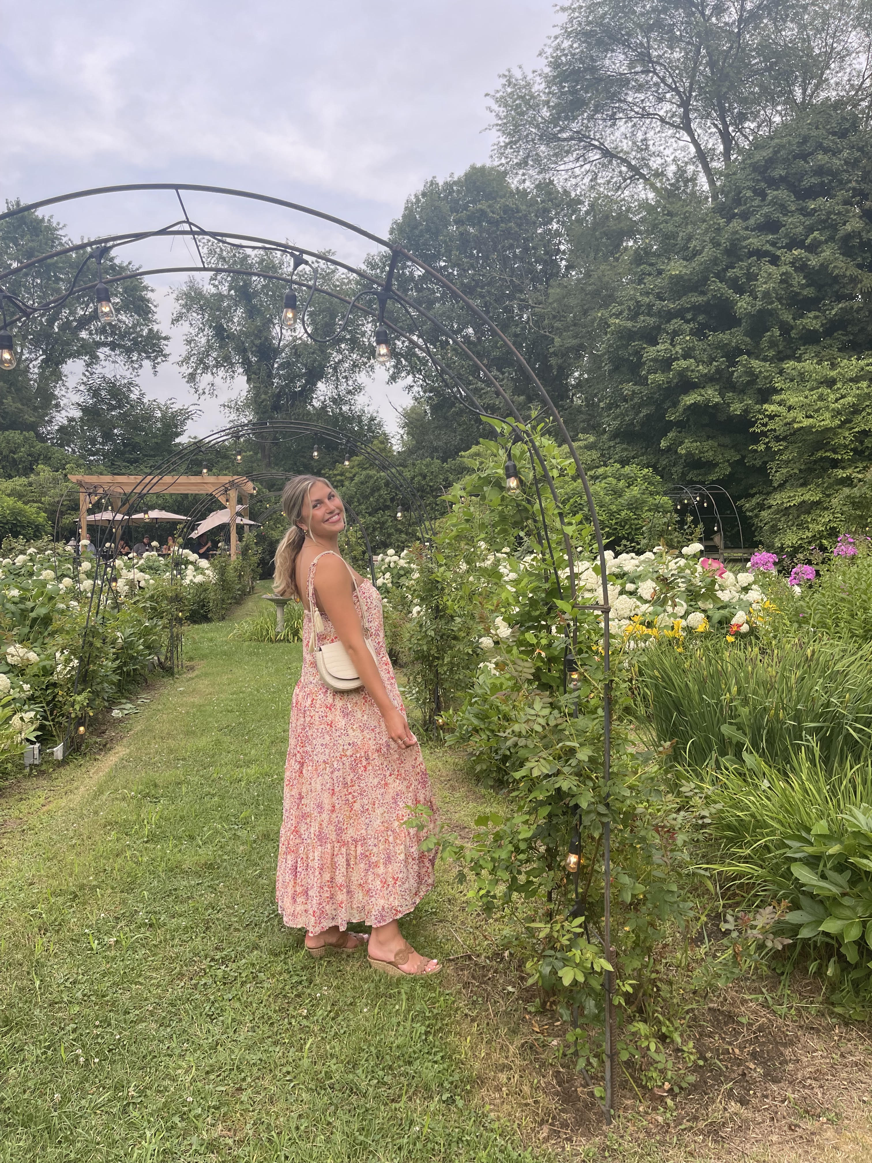 Emma Hochstein in a long floral dress smiling in a garden